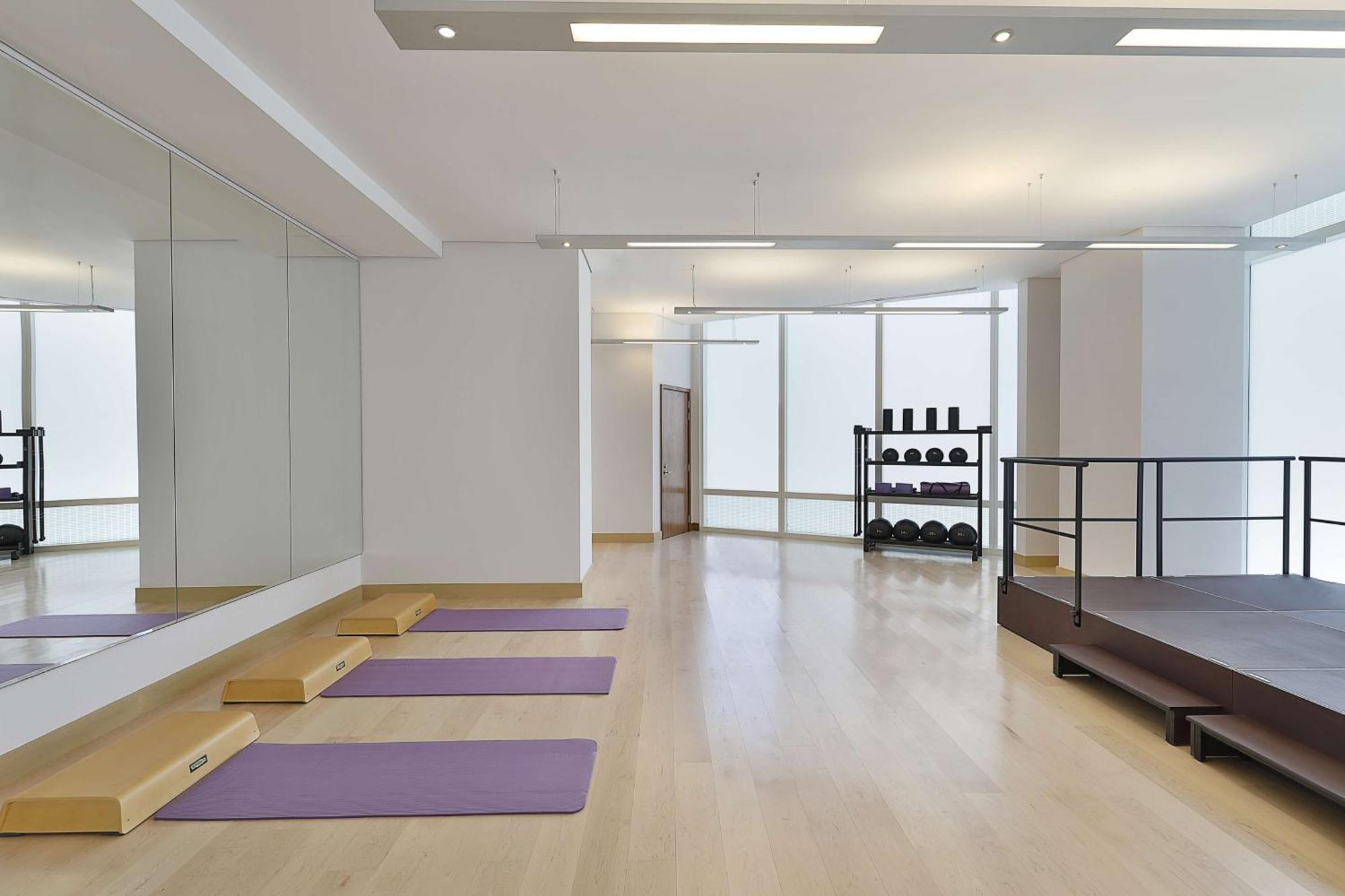Hilton Riyadh Hotel & Residences Kültér fotó The photo depicts a spacious exercise or workout studio. It features wooden flooring and a large mirror on one wall. There are three purple yoga mats neatly placed on the floor, and a small set of wooden steps beside them. In the background, there is