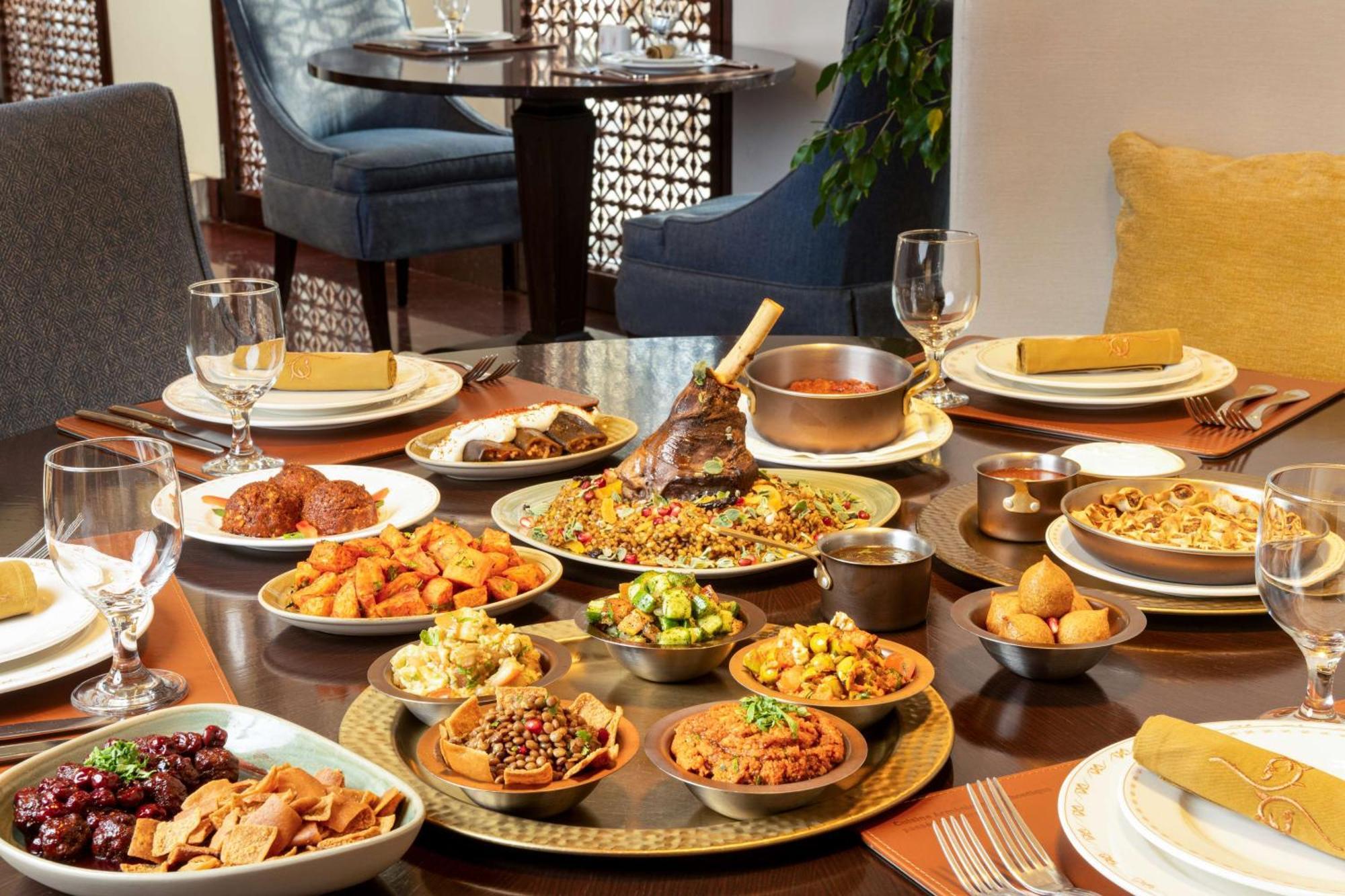 Hilton Riyadh Hotel & Residences Kültér fotó The photo depicts a beautifully arranged dining table featuring a variety of dishes. There are several large plates filled with different foods, including a prominent dish at the center that appears to be rice and meat, likely a type of biryani or pi