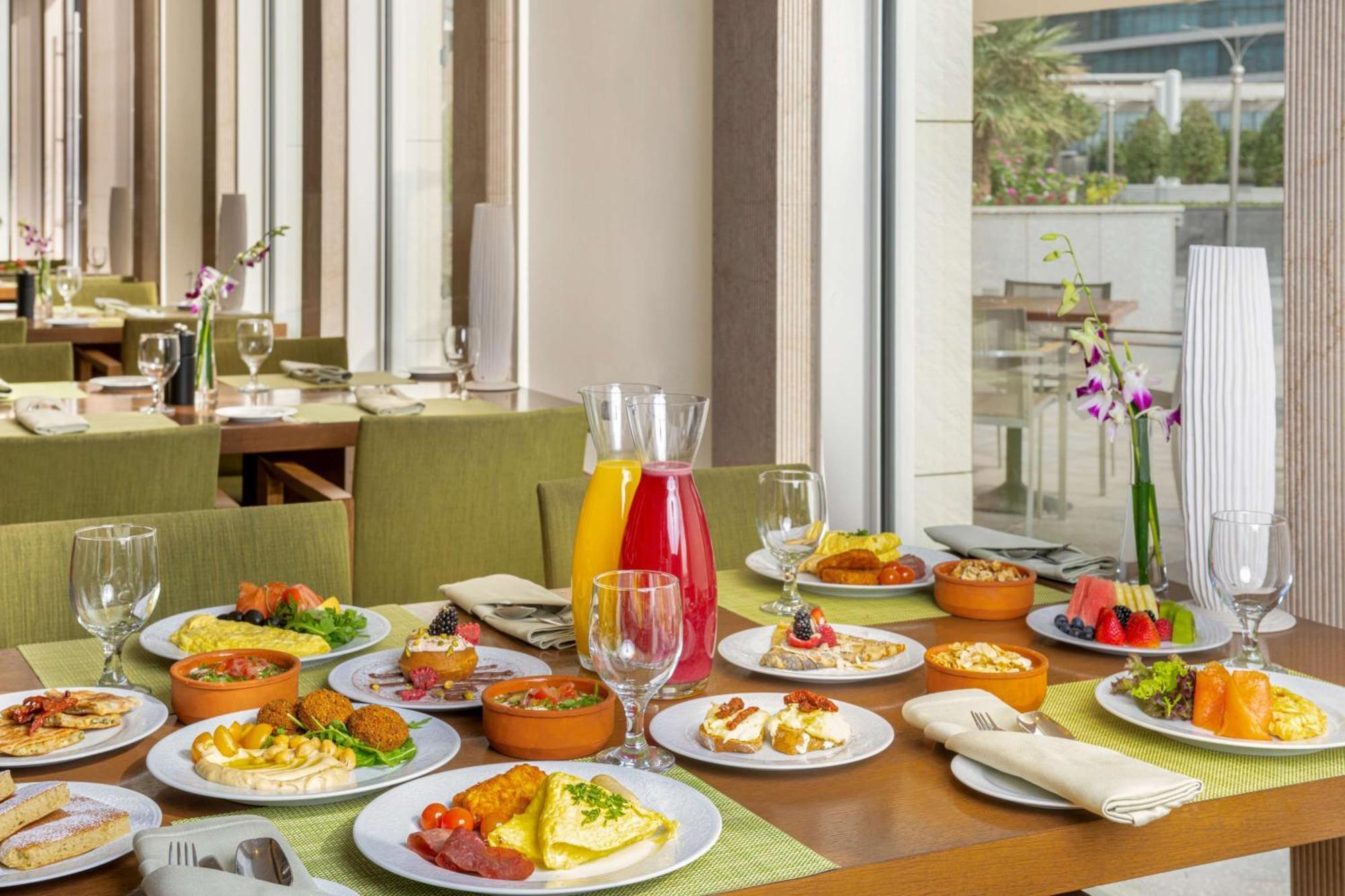 Hilton Riyadh Hotel & Residences Kültér fotó The photo showcases a beautifully arranged dining table filled with a variety of dishes. There are multiple plates featuring an assortment of foods, including salads, appetizers, and main courses, presented in a vibrant and appetizing manner. Additio